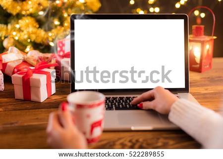 Detail of woman hand working on laptop with empty screen on wooden table. Blur Christmas tree and gifts on background