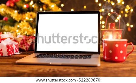 Laptop with empty screen on wooden table, blur Christmas tree and gifts on background