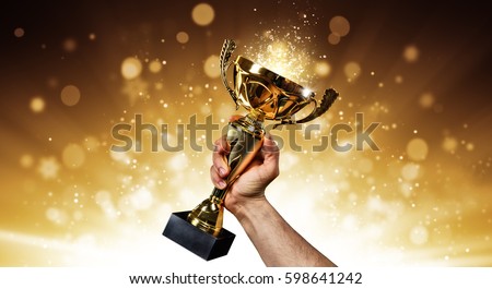 Man holding up a gold trophy cup with abstract shiny background, copy space for text