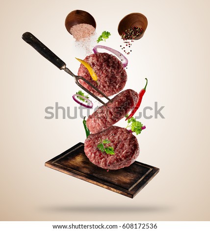 Flying raw milled hamburger meats pieces, with ingredients for cooking. Freeze motion. Fork holding the meat. Concept of food preparation in low gravity mode. Separated on smooth background