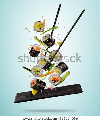 Flying sushi pieces served on plate, separated on colored background. Many kinds of popular sushi food with chopsticks. Concept of flying asian dish with ingredients