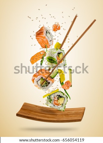 Flying sushi pieces served on plate, separated on colored background. Many kinds of popular sushi food with chopsticks. Concept of flying asian dish with ingredients