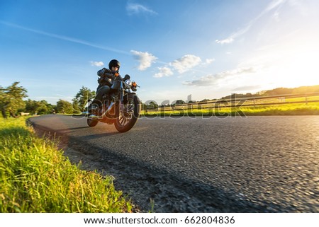 Dark motorbiker riding high power motorbike in nature with beautiful sunset light. Travel and transportation. Freedom of motorbike riding