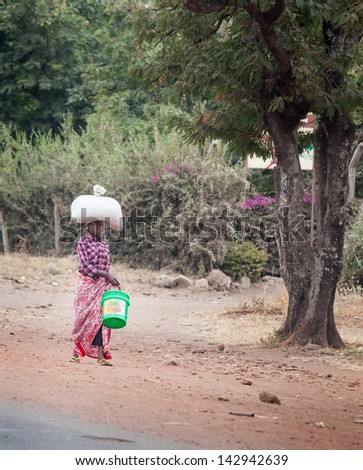 ARUSHA, TANZANIA, AFRICA - July 21: African woman carries sack on her head and bucket for water in poverty stricken area on July 21, 2012  in Arusha, Tanzania in Africa