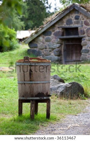 Water bucket with rain water stands in front of stone sod-roofed spring cellar in Skansen, Stockholm, Sweden