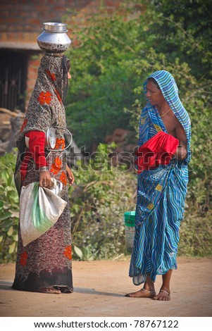 ANAND BAGH, INDIA - NOVEMBER 12-  Typical sari wearing village women converse on dusty dirt street while carrying water containers on their head on November 24, 2010 in Anand Bagh, India.