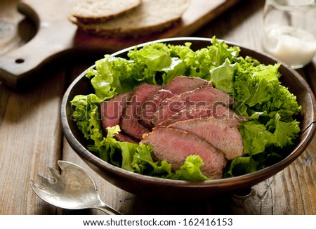 Closeup of a fresh green salad with sliced seared tenderloin steak.