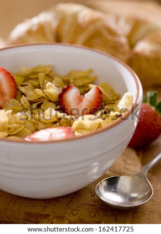 Closeup of a bowl of corn flakes cereal with fresh strawberries.