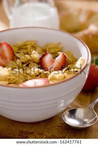 Closeup of a bowl of corn flakes cereal with fresh strawberries.