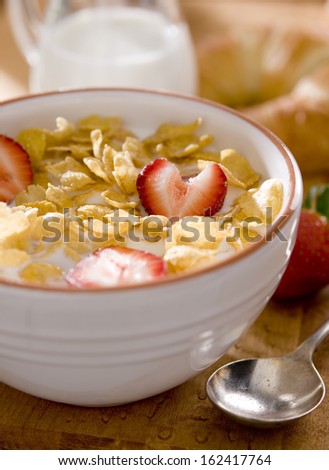 Closeup of a bowl of corn flakes cereal with fresh strawberries and milk.