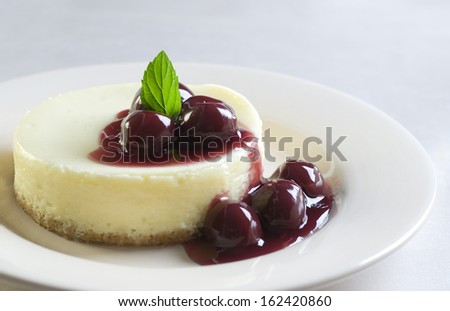 Mini cheesecake with dark cherries in elegant setting.