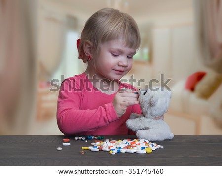 A child plays with pills. Girl feeds pill capsule toy - polar bear cub. Danger game with pills. Bad game. The risk of poisoning