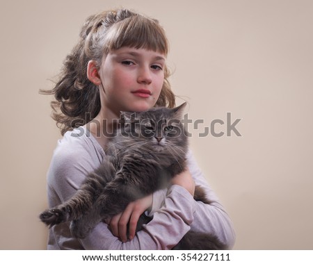 Portrait of a girl with a cat. Young, beautiful girl hugging cat. Cat likes to caress the cat likes to lie in the hands of man. Cat gray, fluffy. Background beige.