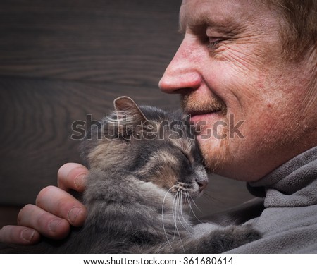 Man and cat - two profiles. Muzzle of a cat and a man\'s face. The man wrinkled. The cat and the owner smile. Cat gently pressed. Love cats and humans. Relationship, weasel. Background - a wooden board