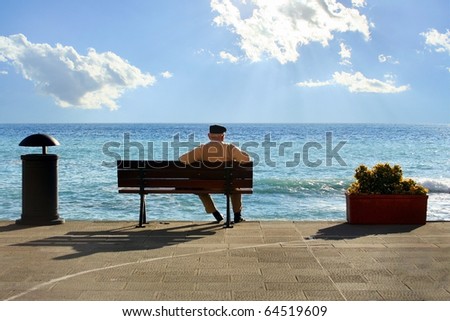 Senior citizen man sitting on a bench and watching the sea and clouds on a beautiful day in Italy