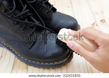 Shoe brush polishes toe cap of boot by one hand on wood floor