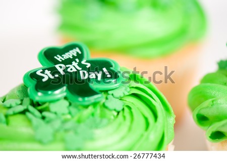 Cupcake with green icing and Happy St-Pat\'s Day written on it. It is on a white background with other cupcakes in the background.