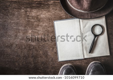 Opened old blank book with magnifying glass. Detective hat and shoes on brown background. Retro things. Historical atmosphere. Vintage english style. Evidence searching concept. Empty place for text.