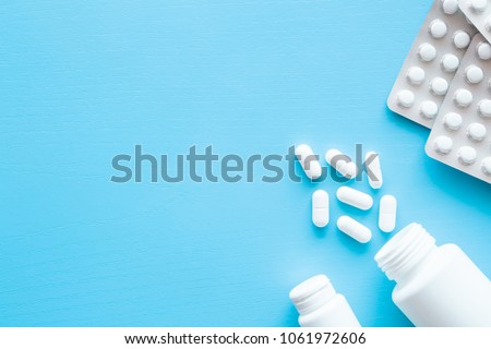 Pills spilled out of white bottle on blue background. Mock up for special offers as advertising or other ideas. Medical, pharmacy and healthcare concept. Copy space. Empty place for text or logo.