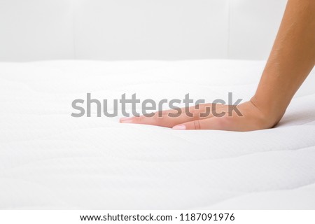 Woman\'s hand pressing on white mattress. Checking hardness and softness. Choice of the best type and quality. Side view. Close up.