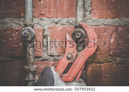 Man\'s hand in protective glove working with wrench at old rusty pipe. Plumbing. Vintage style.