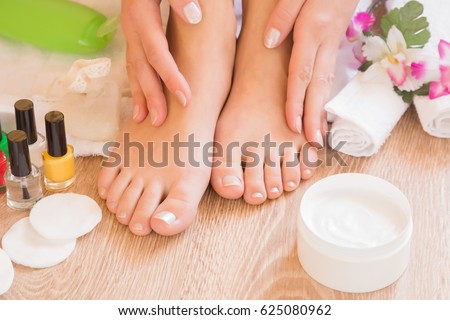 Young woman\'s hands applying a foot moisturizing cream. Pedicure beauty salon.