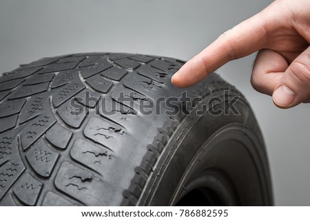 Man\'s hand finger pointing to the old, damaged and worn black tire tread. Change time. Tire tread problems and solutions concept.