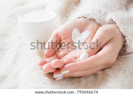 Beautiful groomed woman\'s hands with cream jar on the fluffy blanket. Moisturizing cream for clean and soft skin in winter time. Heart shape created from cream. Love a body. Healthcare concept.