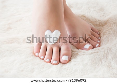 Elegant bare feet. Beautiful groomed woman's feet on the fluffy mat. Cares about clean and soft legs skin in winter time. Heart shape created from cream. Love a body. Healthcare concept.