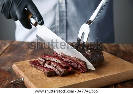 Hands in black gloves slice medium rare cooked whale meat steak with knife and fork