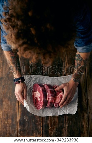 Very top view curly head butcher packing three steaks in paper, focus on steaks, blurred head