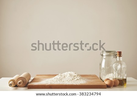 Two wooden rolling pins, extra virgin olive oil, transparent jar and wooden cutting board with white flour, chiken eggs isolated. Everything prepared for dough making