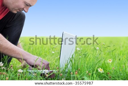 a man on the meadow tipping on the keyboard of a laptop