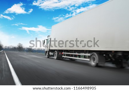 White truck driving fast and a white trailer with space for text on the countryside road against blue sky with clouds