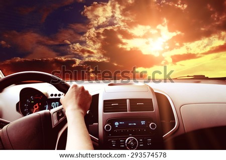 Driver\'s hands on a steering wheel of a car and blue sky with clouds