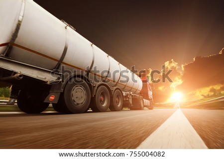 Big metal fuel tanker truck in motion shipping fuel against dark sky with sunset