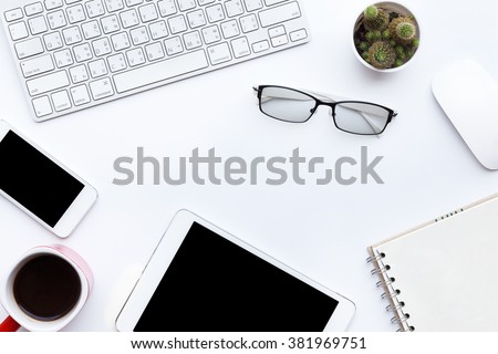 Flat lay photo of office desk with keyboard, notebook, tablet, smartphone, eyeglasses and red cup, top view