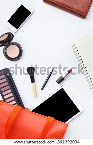 Flat lay of orange woman bag open out with tablet, smartphone, purse, notebook and cosmetics on white background