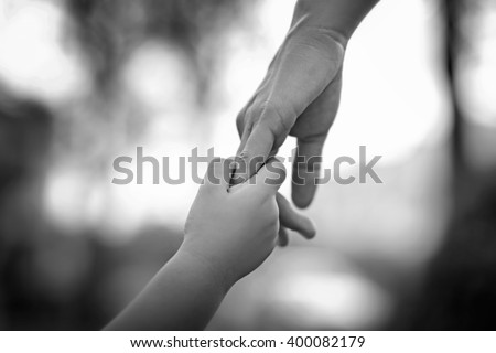 Parent holds the hand of a little child on abstract blur background, soft focus, black and white tone