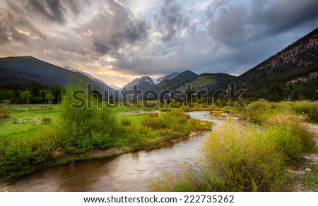 Rocky mountains national park, stream in the foreground and distant mountains with sunset sky and green aspens
