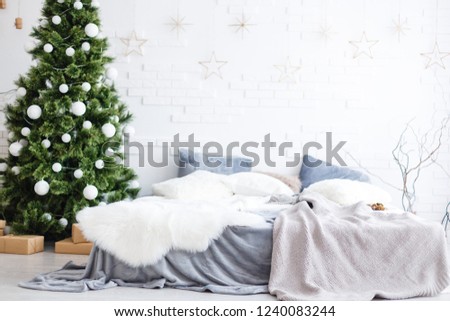 Light Christmas interior room decorated with Christmas tree, gift boxes, white walls and white coverlet. Christmas interiors with bed, fir-tree, pillows.