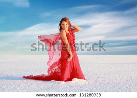 Young woman in red dress with translucent shawl in the snow desert under blue sky