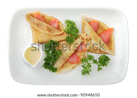 pancakes with salmon and cheese sauce on rectangular white dish isolated on white background