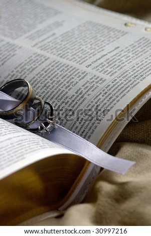 Engagement and wedding rings in ribbon in middle of Bible on a blanket