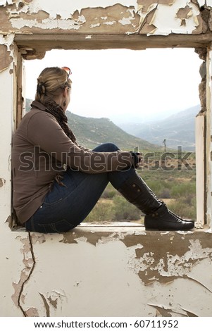 A Beautiful woman sitting and staring out of a window frame of old building