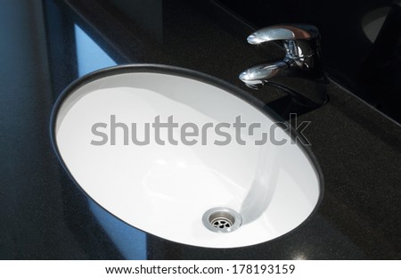 Faucet and white sink in the bathroom with black marble