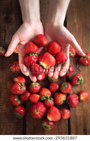strawberry in hand on the background of the table which also strawberries