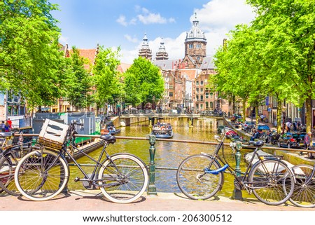 AMSTERDAM, NETHERLANDS - MAY 31, 2014: Tourists walking by a canal in Amsterdam. Amsterdam is the capital of the Netherlands and the canals and harbours fill a full quarter of the city surface.