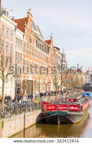 AMSTERDAM, NETHERLANDS - MARCH 7, 2015: Tourists walking by a canal in Amsterdam. Amsterdam is the capital of the Netherlands and the canals and harbours fill a full quarter of the city surface.