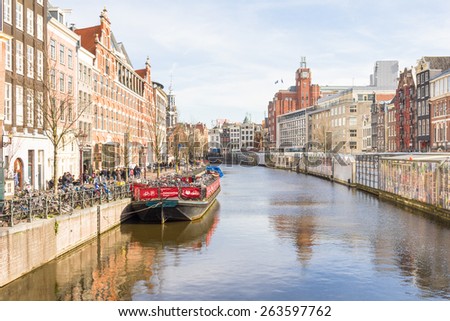 AMSTERDAM, NETHERLANDS - MARCH 7, 2015: Tourists walking by a canal in Amsterdam. Amsterdam is the capital of the Netherlands and the canals and harbours fill a full quarter of the city surface.
